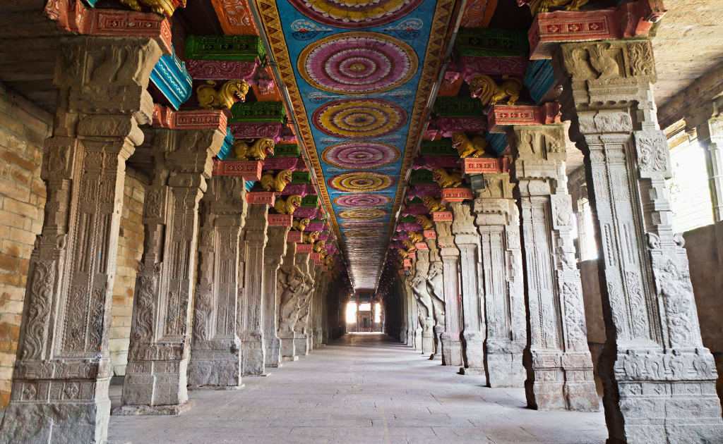 Intricately carved stone pillars and colorful ceiling artwork inside Kamakshi Amman Temple corridor.