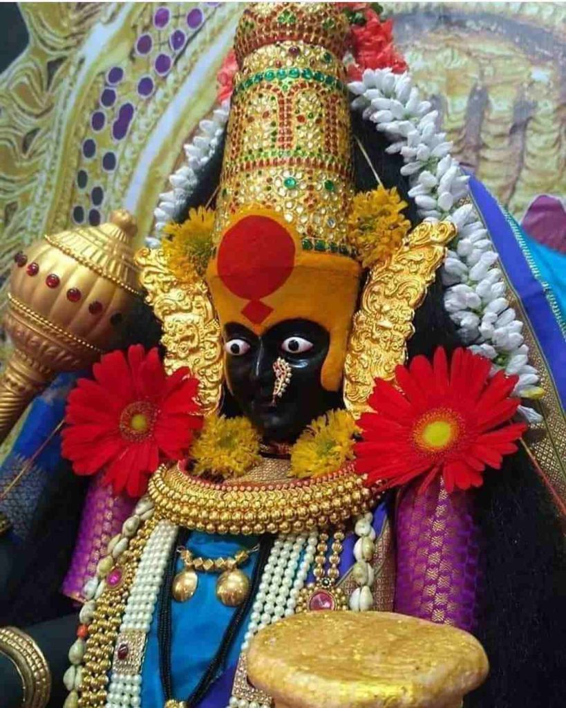 Close-up view of Kolhapur Mahalakshmi idol decorated with flower garlands and gold crown